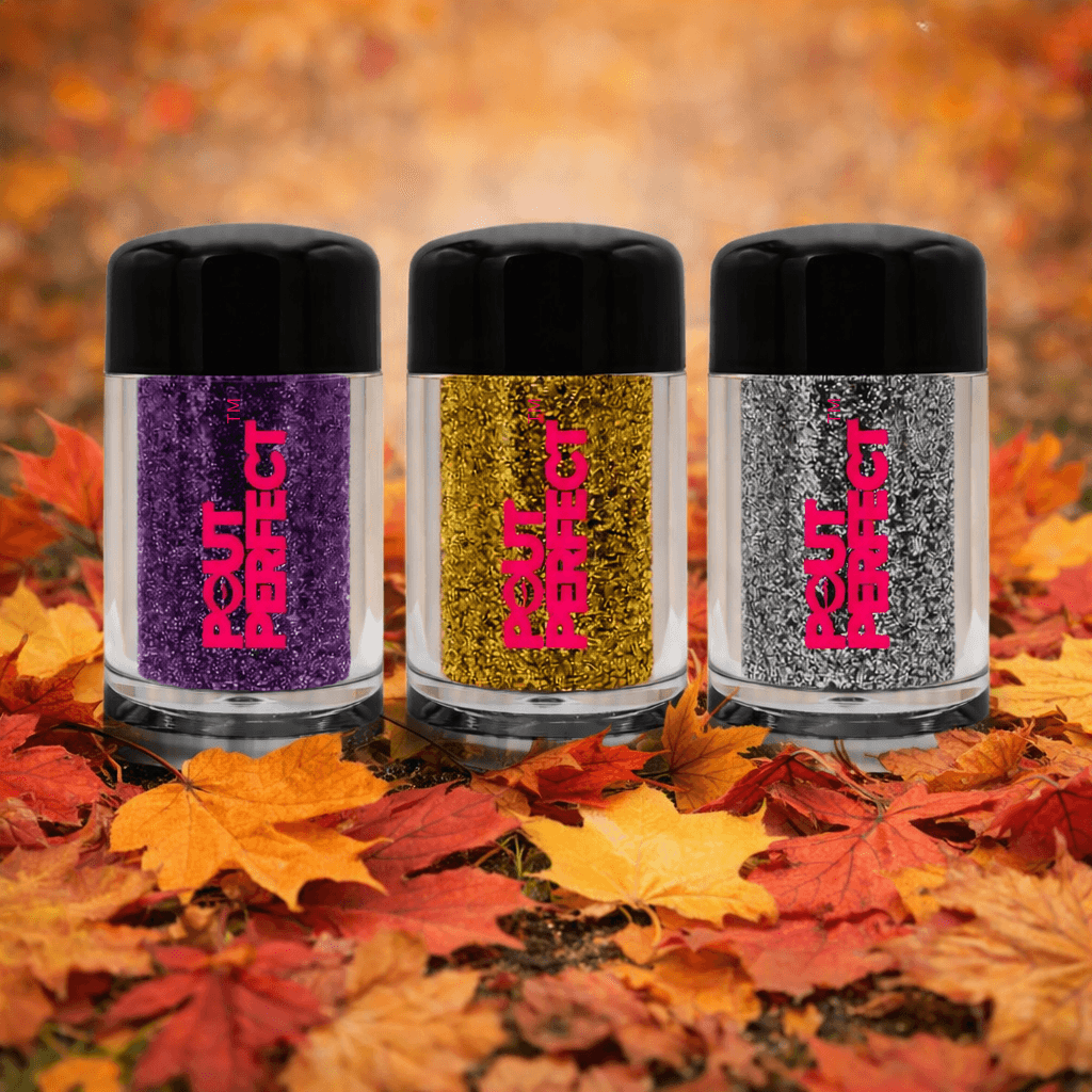 Three clear jars of Four Perfect glitter with black lids are arranged on orange and red autumn leaves. The glitter inside is purple, metallic gold, and silver, with the brand name 'FOUR PERFECT' printed in bright pink on each jar. Perfect Pout Lip Accessories