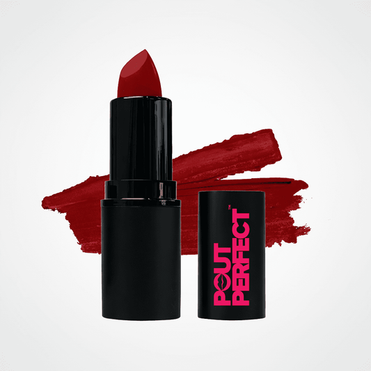 A black lipstick tube with a deep red lipstick bullet standing upright, alongside its matching black cap printed with pink 'OUT OF OFFICE' branding. A textured red lipstick swatch is displayed behind them on a clean white background. Ruby Slippers